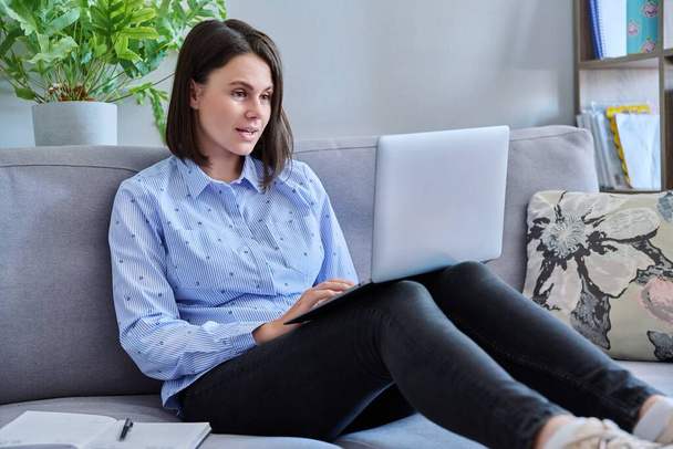 Young business woman working from home using laptop sitting on sofa at living room. Freelance, remote work, online business, technology, sales, e-learning, e-education concept - Fotoğraf, Görsel