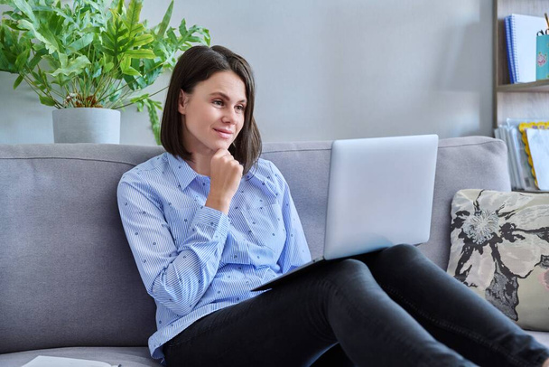 Young business woman working from home using laptop sitting on sofa at living room. Freelance, remote work, online business, technology, sales, e-learning, e-education concept - 写真・画像