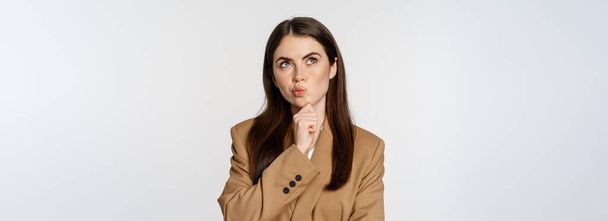 Image of businesswoman thinking, corporate woman looking thoughtful, making decision, standing in brown suit over white background. - Fotó, kép