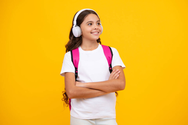 Schoolgirl, teenage student girl in headphones on yellow isolated studio background. School and music education concept. Back to school - Foto, Imagem