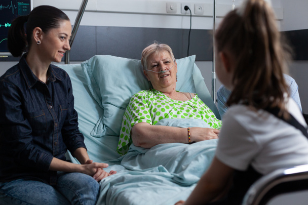 Malá holčička navštěvuje babičku v nemocnici. Žena s dcerou doprovázející starší dámu ležící v posteli v sanatoriu. Stará pacientka odpočívající na geriatrické klinice - Fotografie, Obrázek
