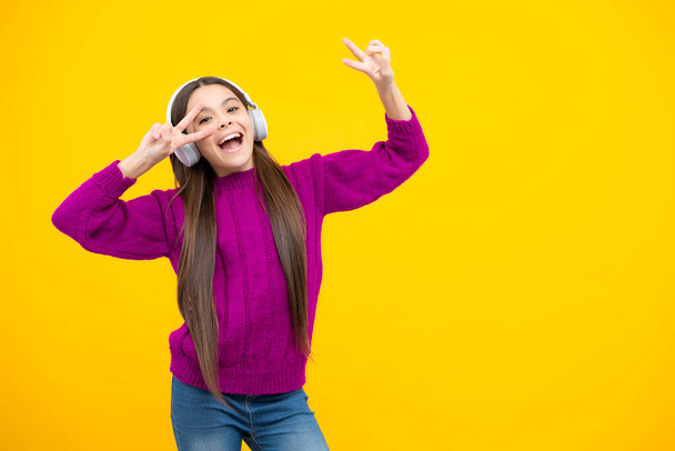 Excited face. Teenager child girl in headphones listening music, wearing stylish casual outfit isolated over yellow background. Amazed expression, cheerful and glad - Photo, image