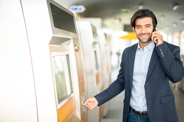 The caucasian man uses a transport card at the ticket machine for travel by sky train in the rush hour time while he uses a smartphone for talking with his friend. - Φωτογραφία, εικόνα
