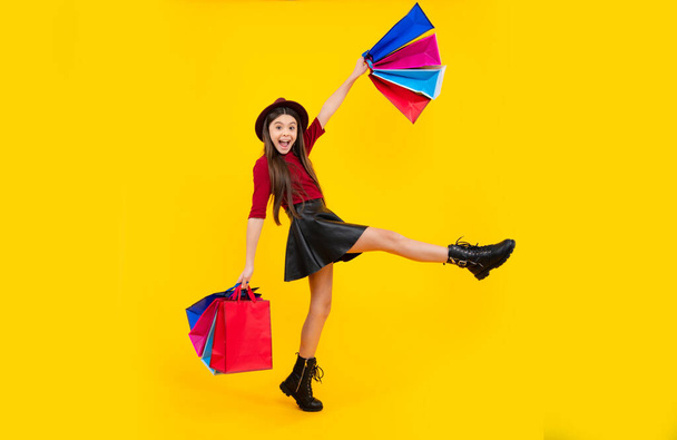 Kind Mädchen halten Einkaufstasche genießen Verkauf isoliert auf gelbem Hintergrund. Porträt von Teenager-Mädchen ist bereit, einkaufen zu gehen. Laufen und springen - Foto, Bild