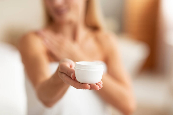 Caucasian woman holding jar of body cream, applying skin care product after shower at home, selective focus, closeup. Sensual mature lady using cosmetics in morning, indoors - Valokuva, kuva