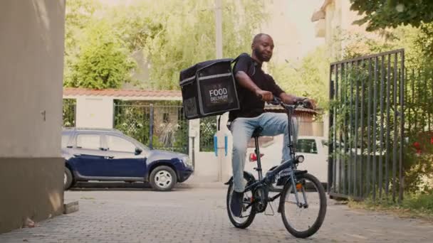 Livraison mâle courier vélo d'équitation avec sac à dos thermique pour donner fastfood paquet de commande aux clients. Aller à l'entrée de la porte d'entrée pour livrer le repas à emporter, service de livraison de restaurant. - Séquence, vidéo