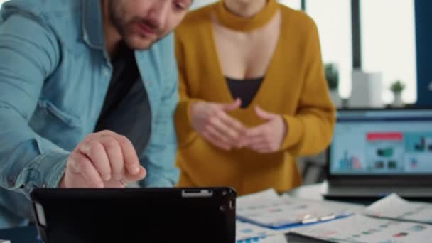 Team of two coworkers looking at tablet with data charts on desk and talking about business strategy standing in startup office. Employee explaining to woman colleague sales plan on digital device. - Filmmaterial, Video