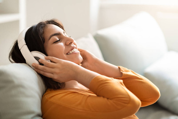 Calm Smiling Young Arab Woman In Wireless Headphones Listening Music At Home, Closeup Shot Of Happy Middle Eastern Lady Relaxing On Couch With Closed Eyes, Enjoying Favorite Playlist, Side View - Photo, Image