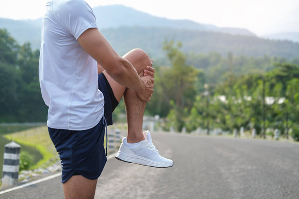 Tiro cortado de homem em roupas esportivas esticando as pernas, aquecendo antes do treino no parque. - Foto, Imagem