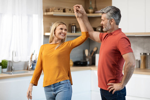Beautiful middle aged spouses dancing together at kitchen, happy handsome man having romantic evening with his beautiful blonde wife at home, copy space. Relationship, marriage, family - Foto, Imagem