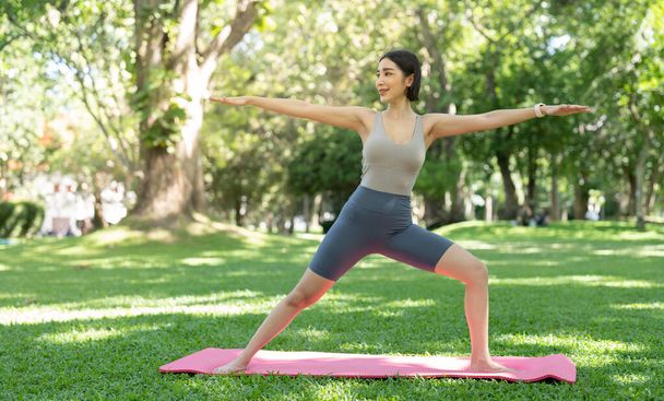 Genç ve çekici bir kız, parkın ortasında spor minderinin üstünde yoga yapıyor. - Fotoğraf, Görsel