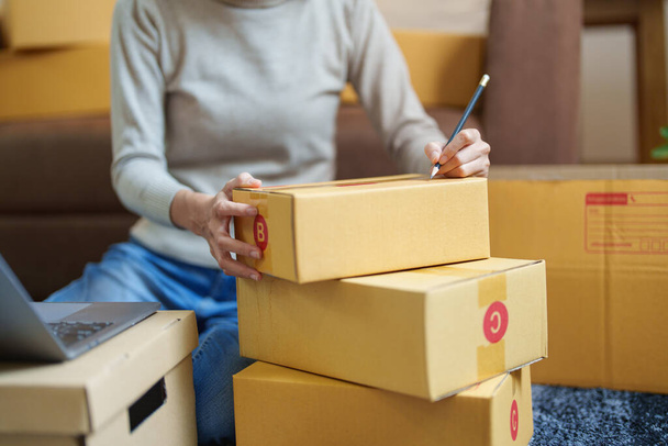 A portrait of a small startup, and SME owner, an Asian female entrepreneur, is writing down information on a box to organize the product before packing it into the inner boxes for the customer. - Photo, image