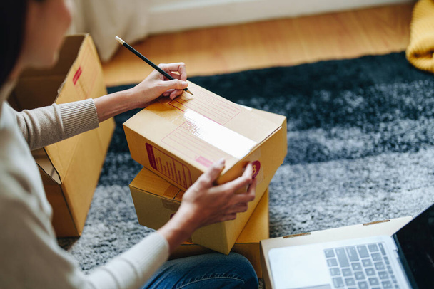 A portrait of a small startup, and SME owner, an Asian female entrepreneur, is writing down information on a box to organize the product before packing it into the inner boxes for the customer. - Photo, Image