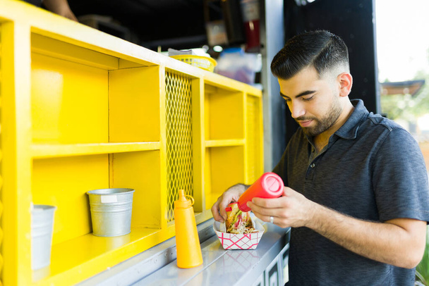 Joven guapo preparando su delicioso sándwich para comer en el camión de comida - Foto, Imagen