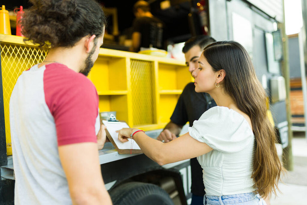 Young woman and friends choosing lunch while looking at the menu from the food truck - 写真・画像