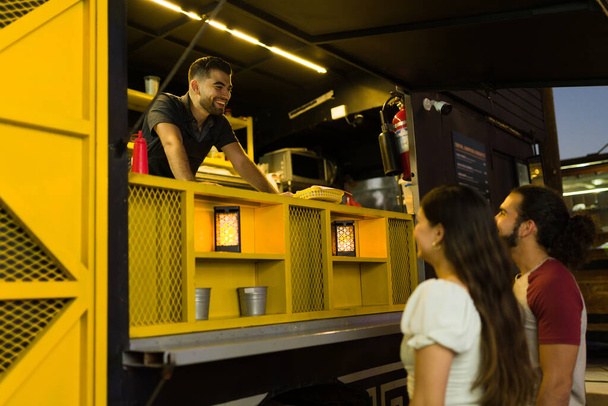 Lavoratore eccitato camion cibo ridendo e cercando felice parlando con i clienti che ordinano fast food  - Foto, immagini