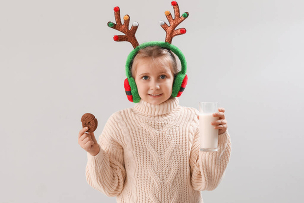 Joyeux petite fille en cornes de rennes avec cookie et verre de lait sur fond clair - Photo, image