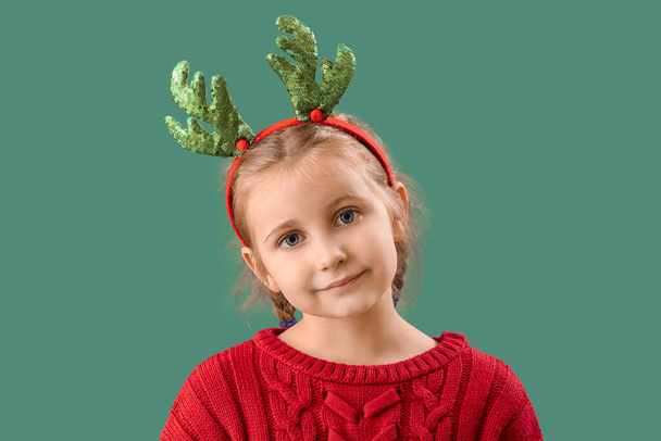 Happy little girl in reindeer horns on green background, closeup - Fotó, kép