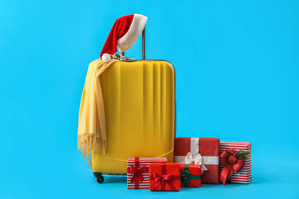Koffer met kerstmuts en kerstcadeaus op blauwe achtergrond - Foto, afbeelding