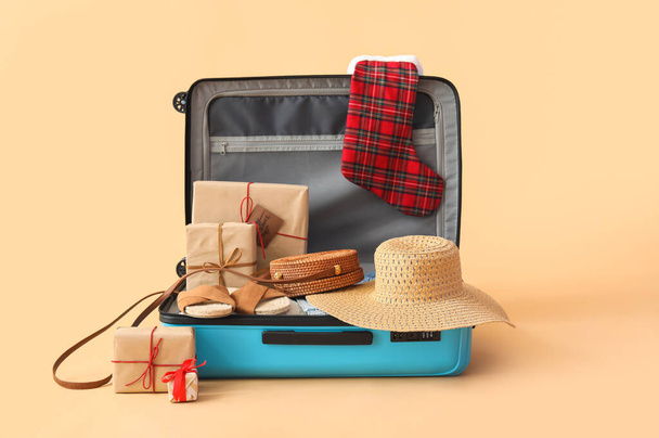 Maleta abierta con accesorios de viaje, calcetines de Navidad y regalos sobre fondo beige - Foto, imagen