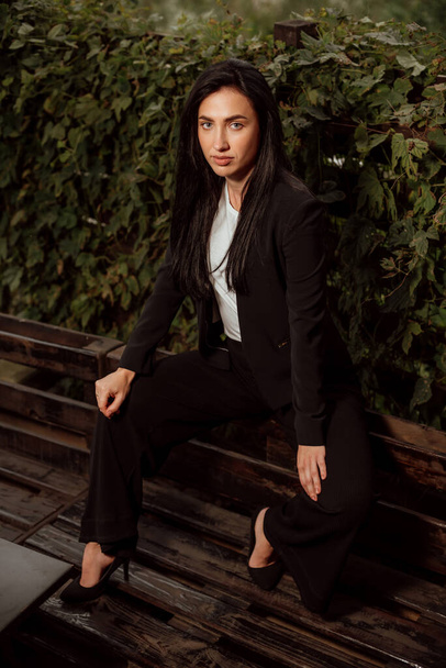beautiful girl with black hair dressed in a black business suit on the street - Foto, Imagen