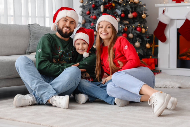 Ευτυχισμένοι γονείς με τον μικρό τους γιο με τα καπέλα του Αϊ Βασίλη να κάθονται σπίτι παραμονή Χριστουγέννων - Φωτογραφία, εικόνα