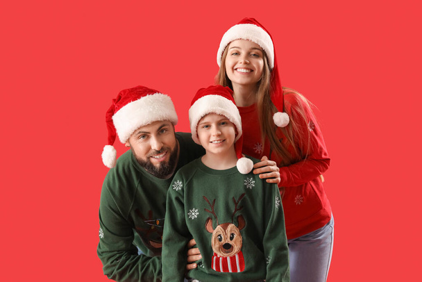 Padres felices con su hijo pequeño en sombreros de Santa sobre fondo rojo - Foto, imagen