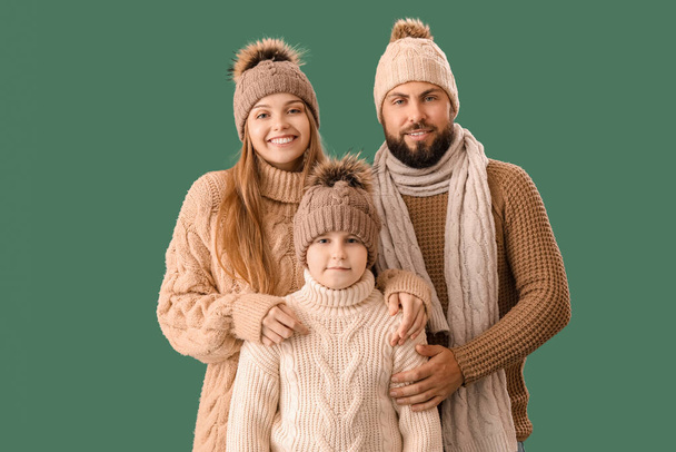 Happy parents with their little son in warm clothes on green background - Photo, Image