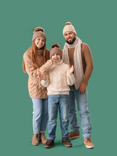 Happy parents with their little son in warm clothes on green background - Fotoğraf, Görsel