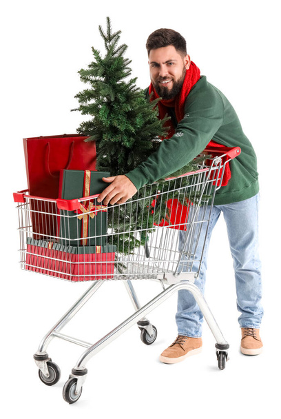 Handsome man with shopping cart, Christmas tree and presents on white background - Fotó, kép
