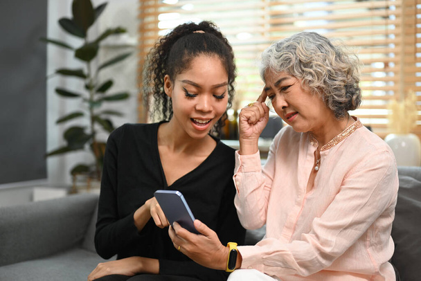 Caring grownup daughter teaching older mother using social networks on smart phone. Elderly, technology concept. - Foto, Bild