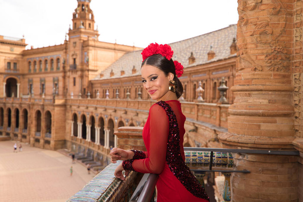 Beautiful teenage woman dancing flamenco on the balcony of a square in Seville. She wears a red dress with ruffles with a lot of art. Flamenco cultural heritage of humanity. - Foto, imagen