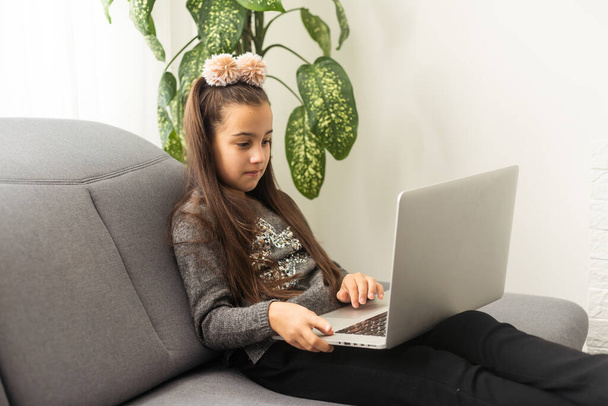 Ηλεκτρονική εκπαίδευση, online μαθήματα και μαθήματα για τους μαθητές. Χαρούμενη έφηβη κοπέλα που κοιτάζει την οθόνη του φορητού υπολογιστή, βλέποντας online μάθημα ή ακούγοντας τον δάσκαλο, εσωτερικό χώρο στο σπίτι, αντίγραφο χώρου. - Φωτογραφία, εικόνα