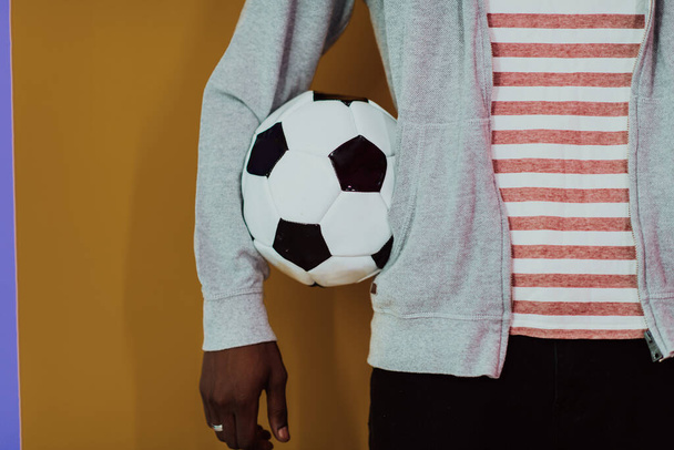 サッカーボールを持ちながら黄色い背景にポーズをとるアフロ男。高品質の写真 - 写真・画像