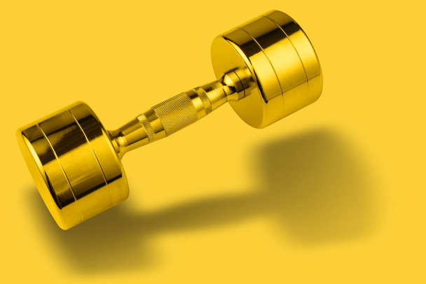 golden shiny dumbbell as if bouncing, casting a shadow, concept on yellow background, copy space - Foto, Imagen