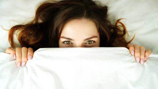 Женщина в постели покрыла лицо одеялом. Понятие бессонницы или страха. Место для вашего текста или объявления - Фото, изображение