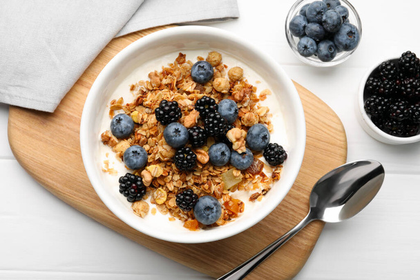 Bowl of healthy muesli served with berries on white wooden table, flat lay - Фото, изображение