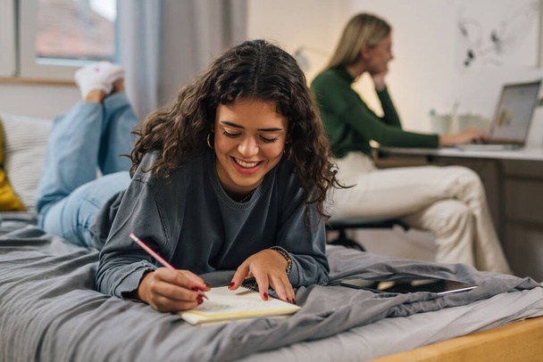 smiling teenager female does home work in dorm room - Photo, Image