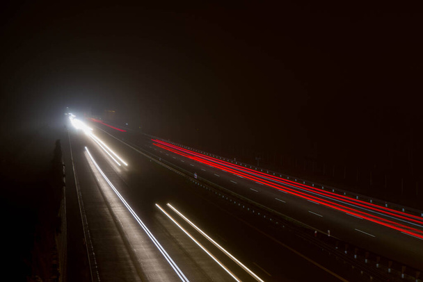 Car light trails at night on a highway seen downwards, long exposure  - Фото, изображение