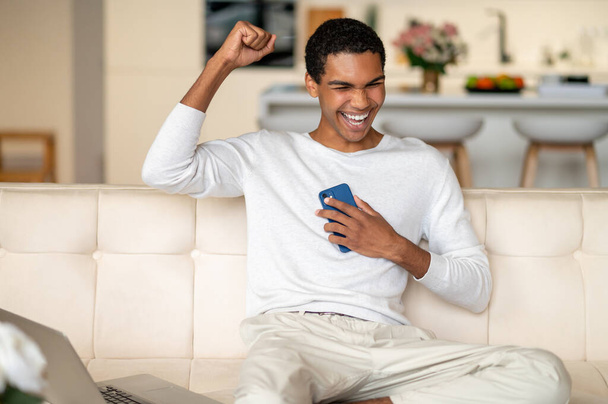 Good mood. Young black man with a smartphone in hands looking happy - Fotó, kép