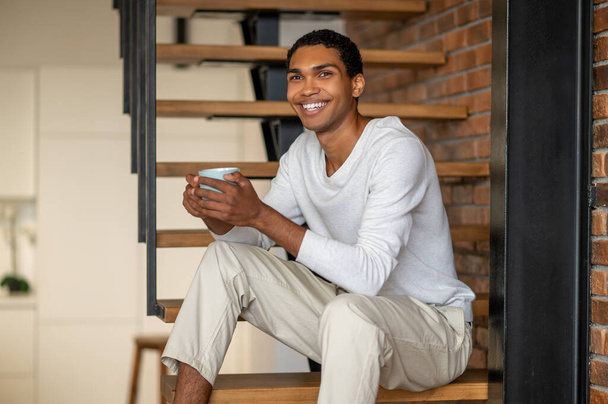 Morning coffee. Young smiling man at home having coffee and looking contented - Foto, afbeelding