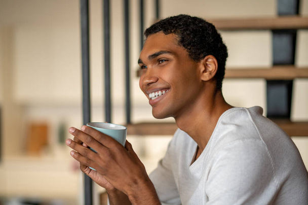 Morning coffee. Young smiling man at home having coffee and looking contented - Foto, immagini