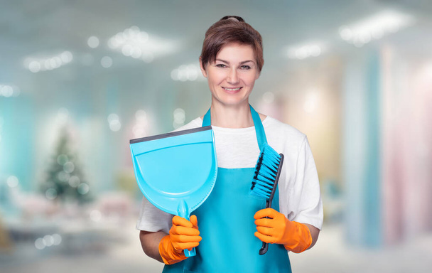 Una donna delle pulizie sta con uno strumento di pulizia sullo sfondo di un interno di Capodanno. - Foto, immagini