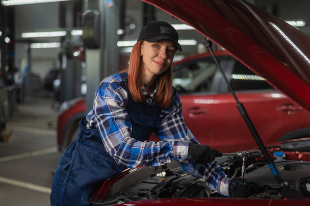 A woman auto mechanic in overalls is repairing a car - Fotoğraf, Görsel