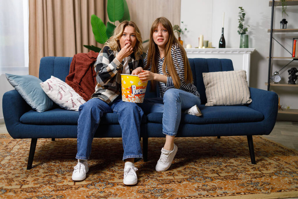 Женщины с удивленными лицами смотрят телевизор дома на диване - Фото, изображение