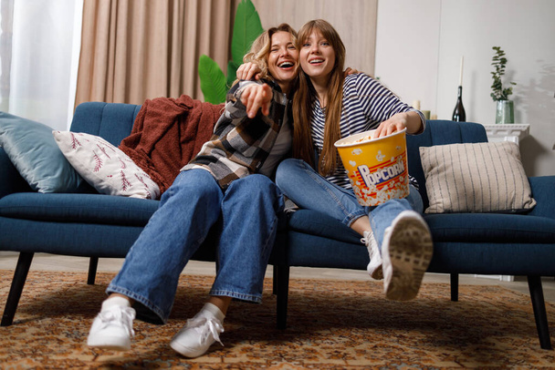 Mujer de mediana edad con su hija adulta divirtiéndose mientras ve la televisión en el sofá del apartamento - Foto, imagen