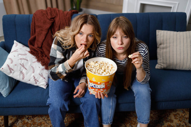Belle ragazze di diverse età sedute sul divano con popcorn e guardando film o show TV interessanti - Foto, immagini
