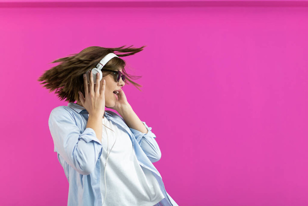 A Brunette lady in black glasses dancing and listening to music isolated on pink background. High quality photo - Foto, afbeelding