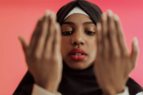 African Muslim woman wearing hijab and traditional Muslim clothes posing in front of a red background.  - Zdjęcie, obraz