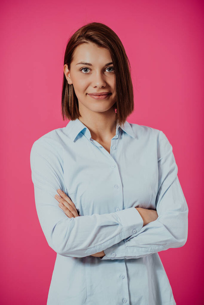Portrait shot of a beautiful blond businesswoman standing with arms crossed on an isolated pink background - Fotó, kép